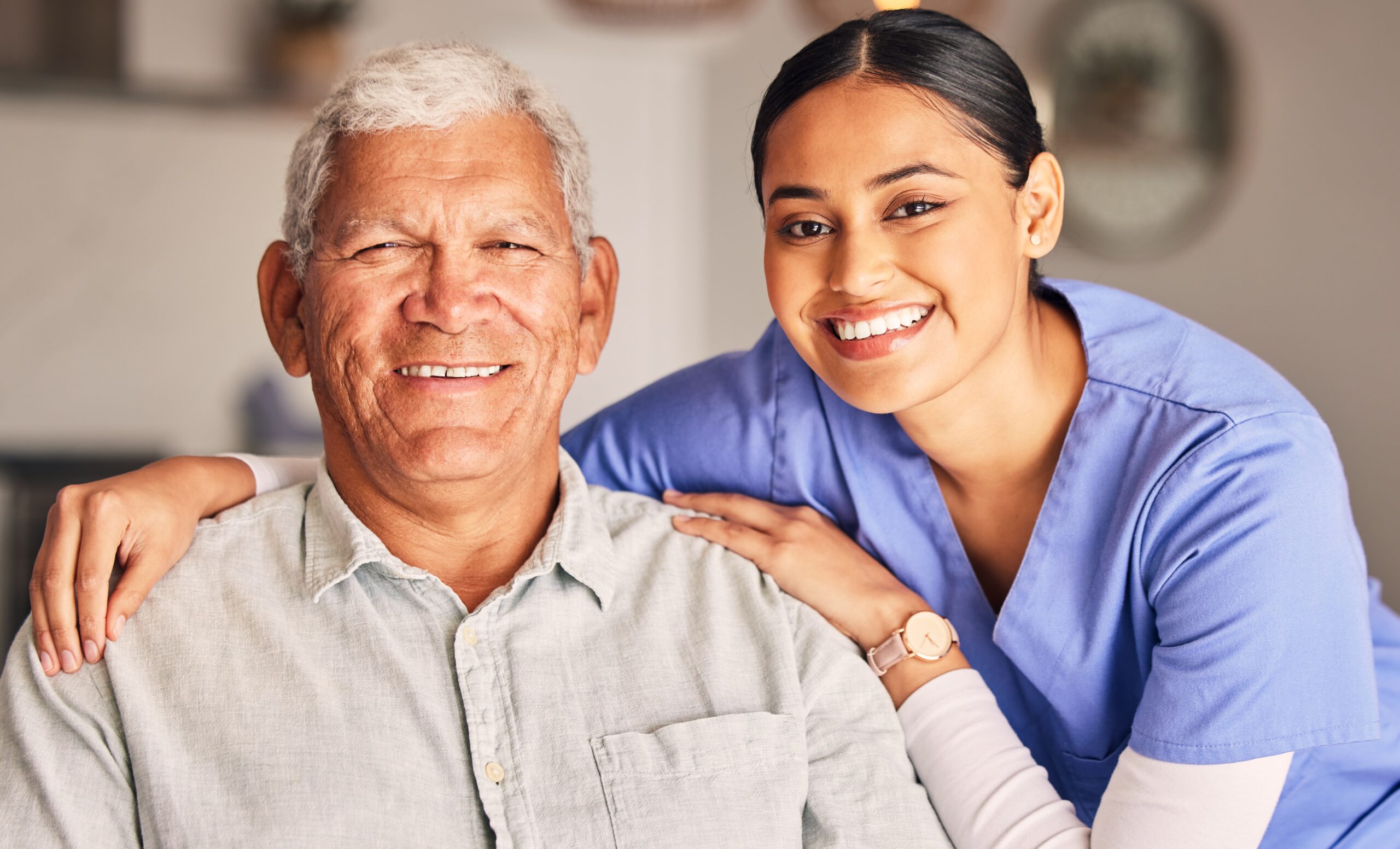 Alastar family senior home care Happy female caregiver and latino senior man embrace and smile in living room Happy female caregiver and latino senior man embrace and smile in living room.